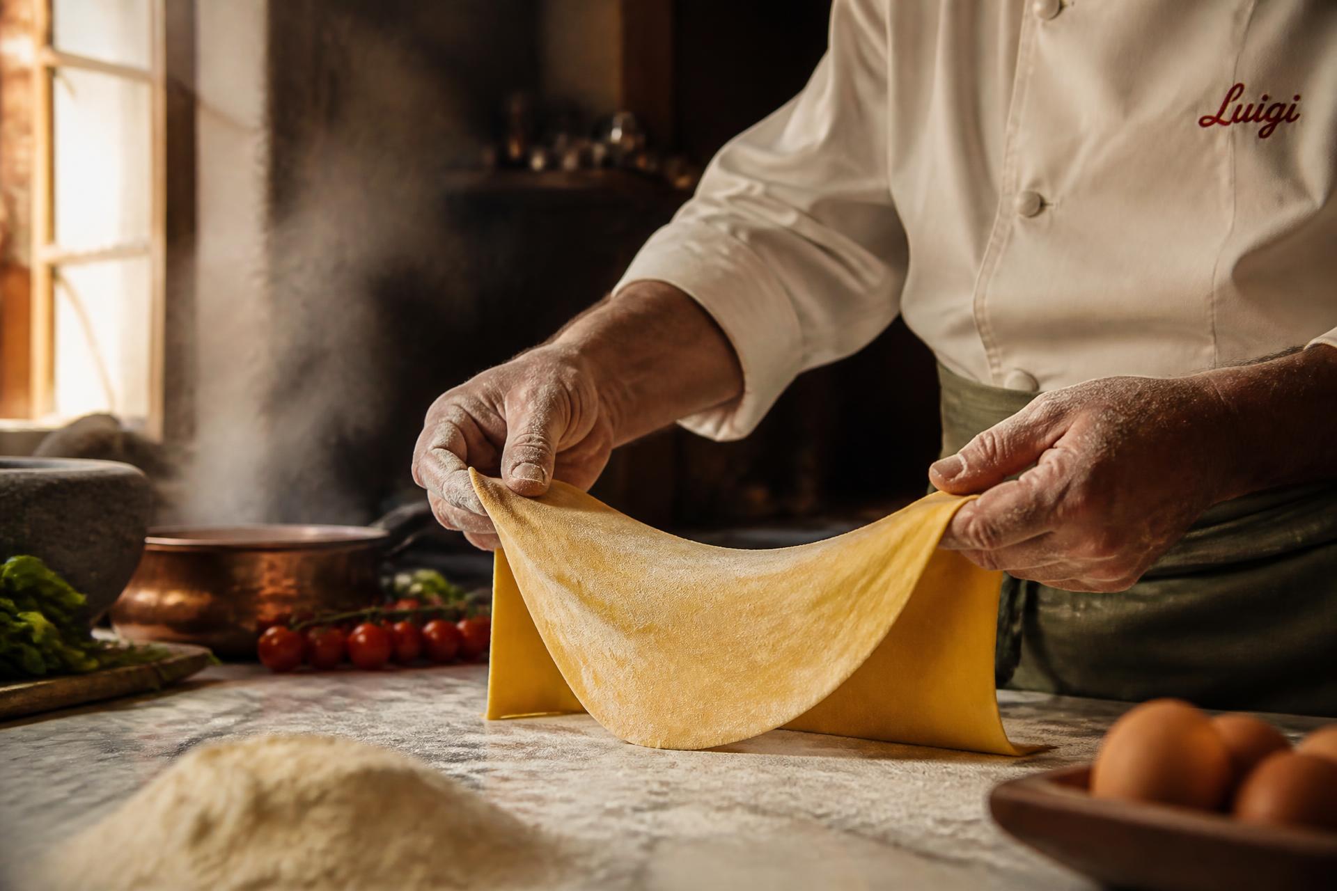 A cook stretching fresh pasta dough in the Sapore kitchen, steam rising behind